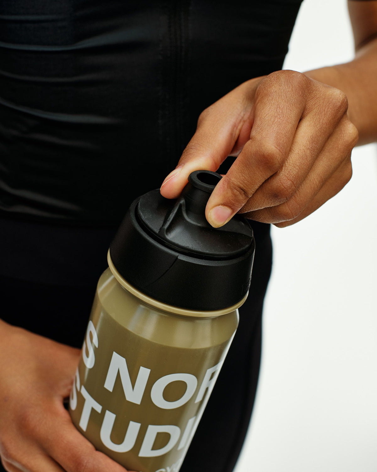 Beige Essential Logo Bidon cycling water bottle, detail view on model with black cap #Color_Beige