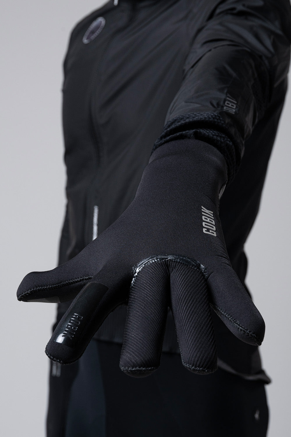 Guantes Gobik Tundra 3.0 en Black, detalle de la mano abierta con los dedos extendidos junto a la chaqueta #Color_Black