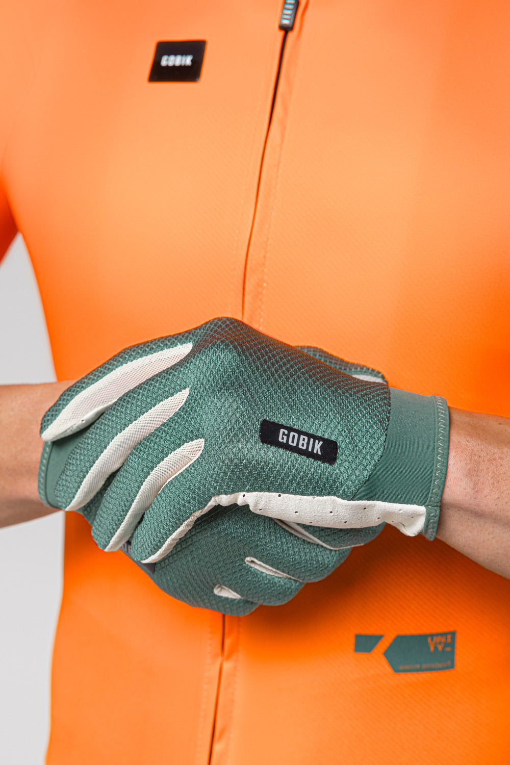 Guantes Gobik Lynx 2.0 en Hedge Green, detalle de las manos con los guantes puestos sobre maillot naranja #Color_Hedge Green