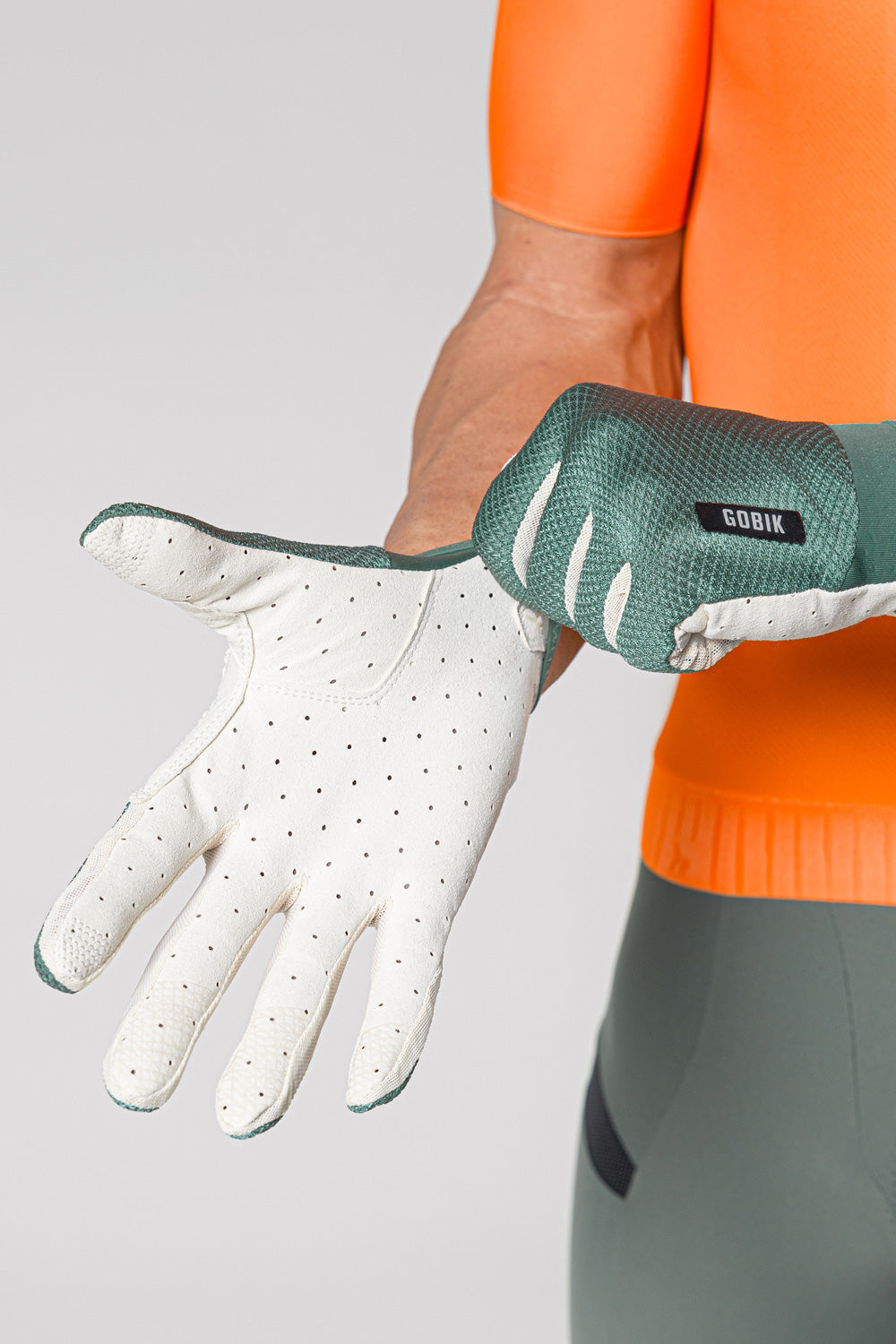 Guantes Gobik Lynx 2.0 en Hedge Green, modelo ajustándose el guante con la palma beige perforada a la vista #Color_Hedge Green