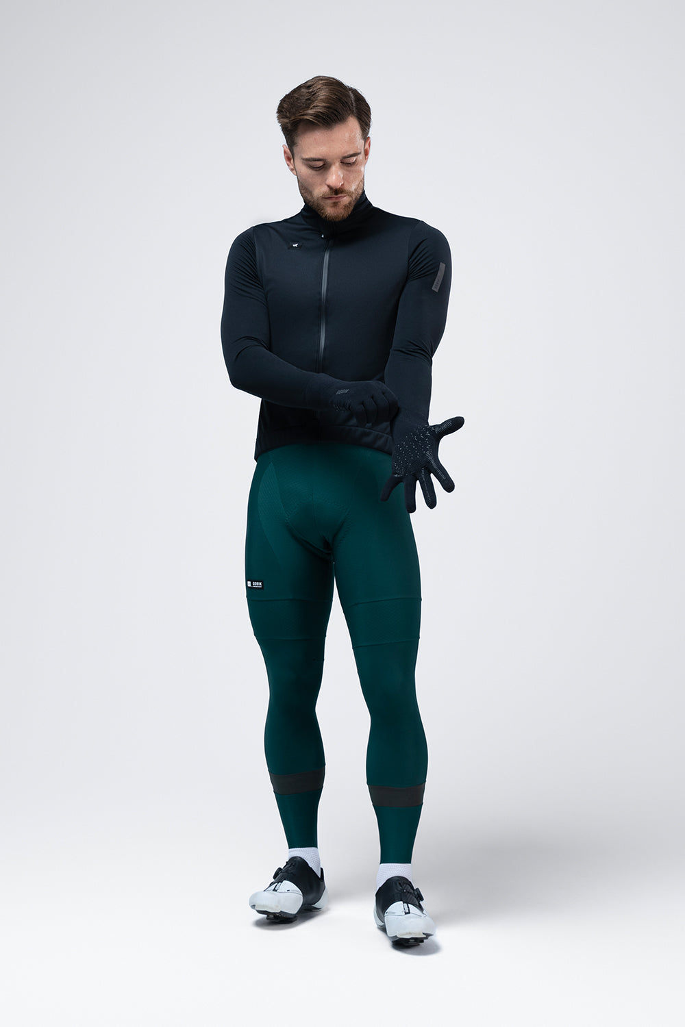 Guantes Gobik Hyperguard en True Black, ciclista de cuerpo entero con ropa de invierno poniéndose los guantes #Color_True Black