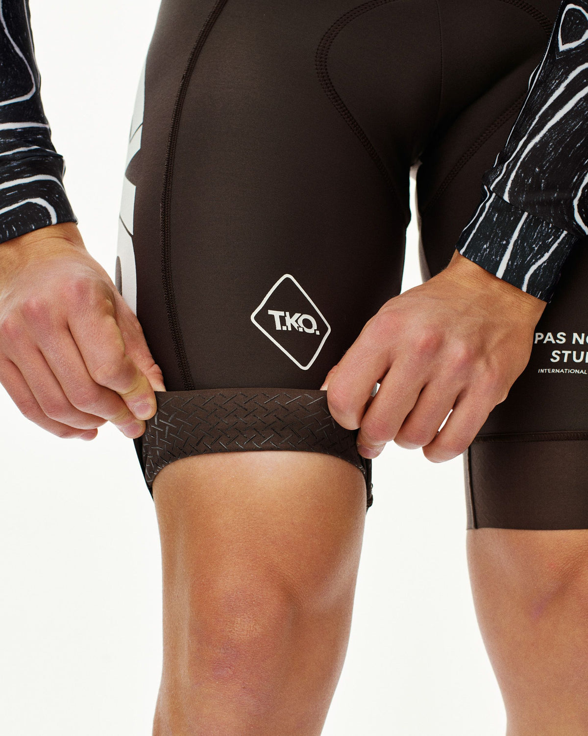 Black T.K.O. Thermal Speedsuit on model, detail view of textured leg gripper band and diamond logo badge #Color_T.K.O. Black Multi