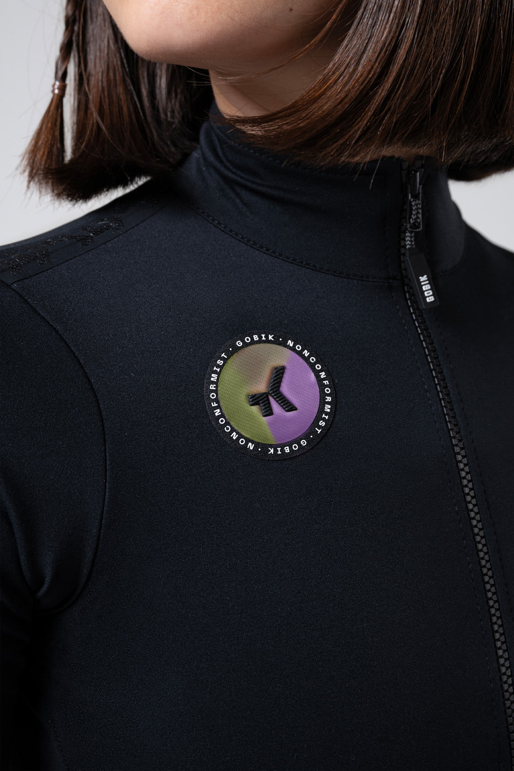 Chaqueta Manga Corta Mujer Gobik Envy 2.0 en Jet Black, detalle del emblema y la cremallera #Color_Jet Black