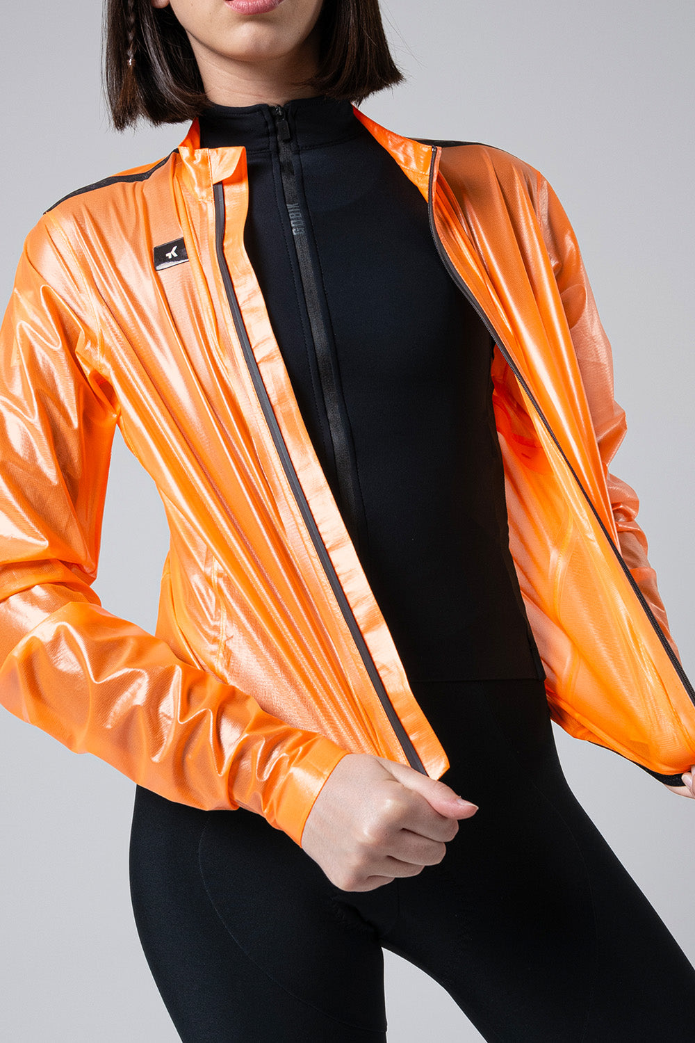 Chaqueta Gobik Pluvia 2.0 en Blazing Orange, detalle del torso abriendo la chaqueta sobre modelo femenino #Color_Blazing Orange