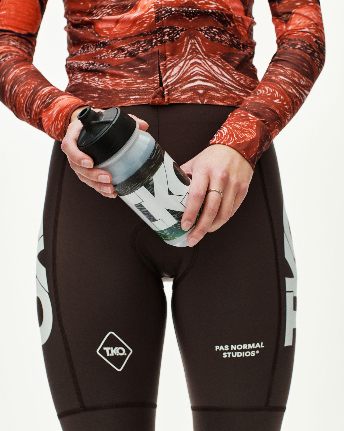 Dark Multi T.K.O. cycling water bottle held by model, front view with graphic print and black cap #Color_T.K.O. Dark Multi