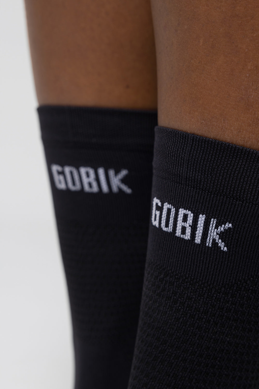 Calcetines Gobik Lightweight 2.0 en Jasper, detalle de las cañas negras con el logotipo Gobik sobre las piernas del modelo #Color_Jasper