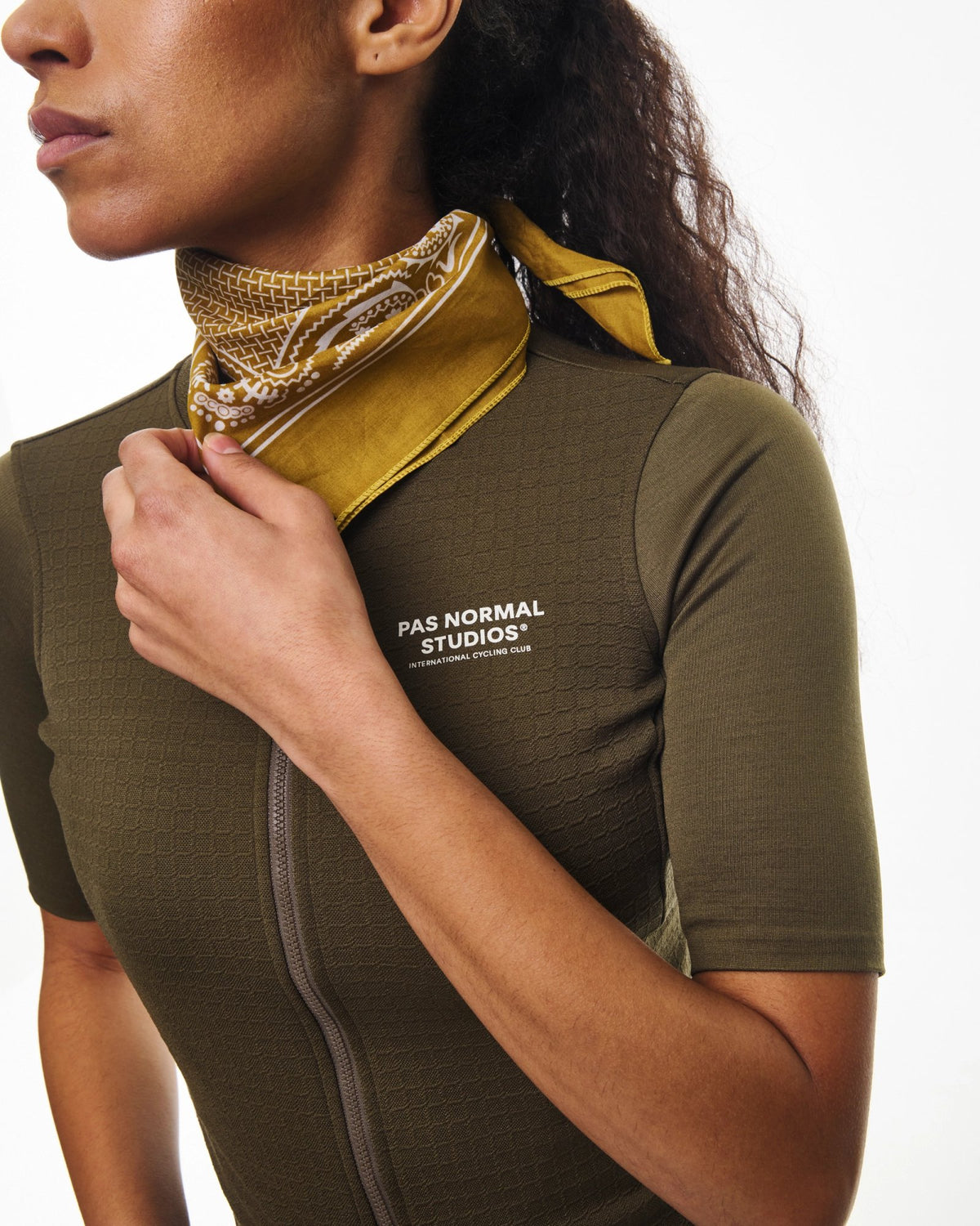 Maillot corto de mujer Pas Normal Studios Escapism Wool en Dark Stone, detalle del cuello sobre la ciclista #Color_Dark Stone