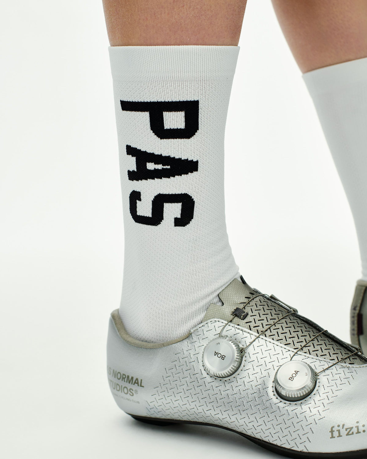 White PAS cycling socks on model with black logo lettering and white road shoes with dual BOA dials #Color_White