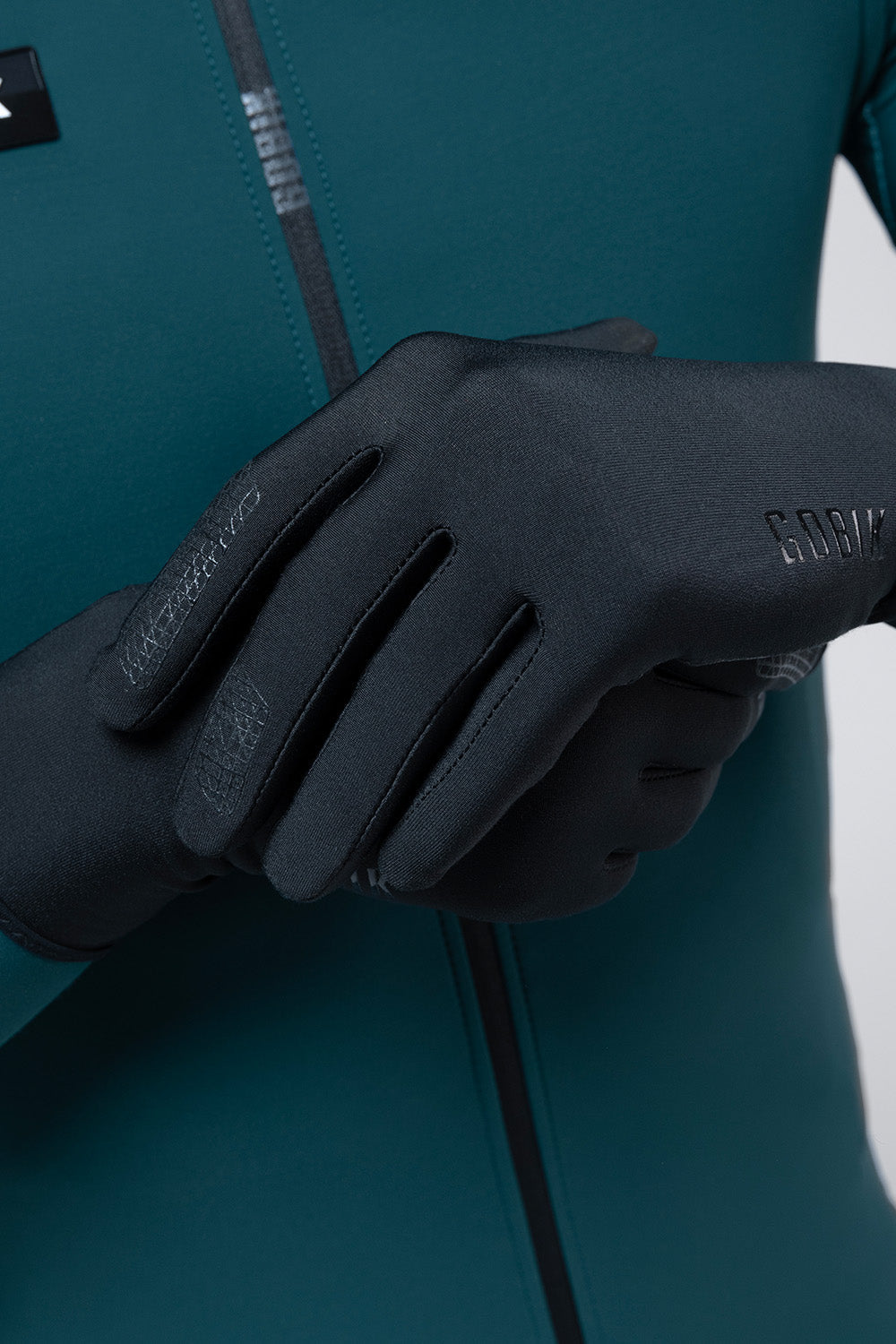 Guantes Gobik Finder 2.0 en True Black, detalle de la mano con el guante puesto sobre el maillot verde #Color_True Black