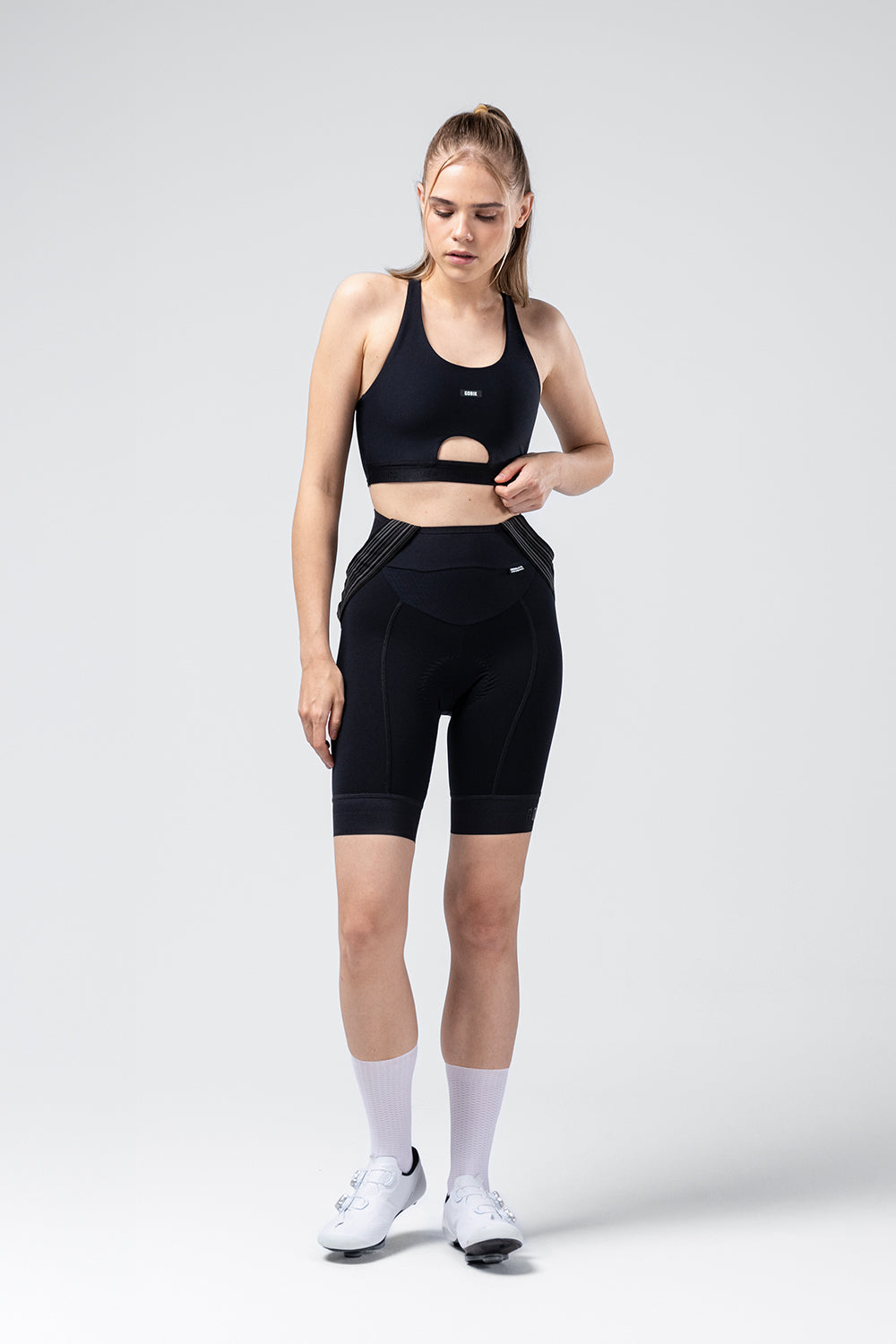 Sujetador Deportivo Gobik Crux en Jet Black, modelo de cuerpo entero ajustándose el culotte #Color_Jet Black